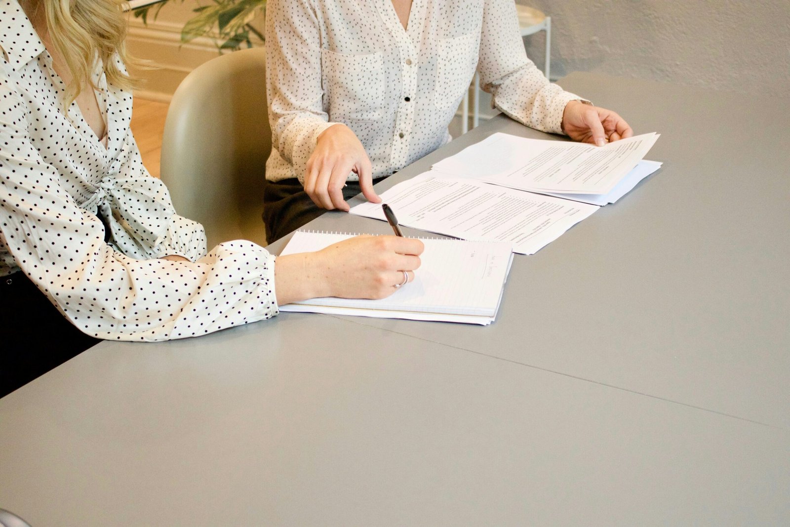 duas mulheres numa mesa com documentos conversando sem mostrar os rostos